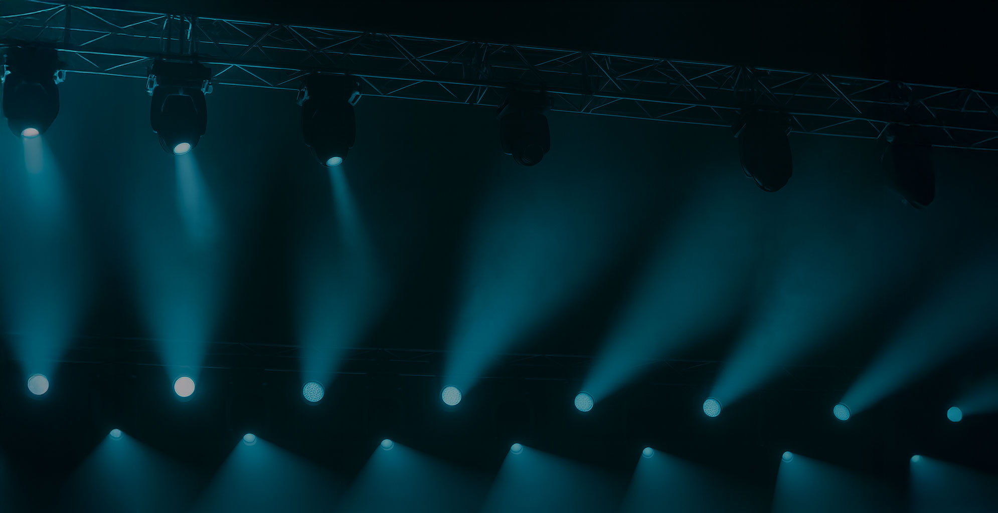 Reihe von Bühnenstrahlern an einer Traverse, die gebündelte Lichtkegel in dunklem Raum nach unten projizieren