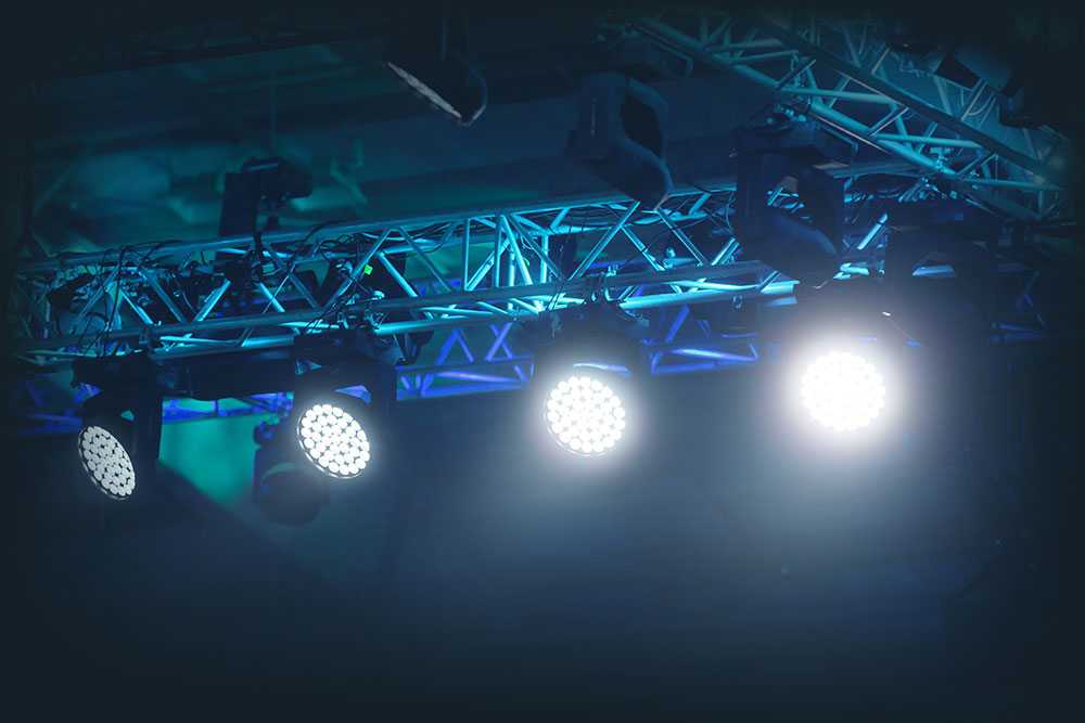 Nahaufnahme einer Traverse mit mehreren hellen LED-Bühnenscheinwerfern und Moving-Lights in blauer Ausleuchtung