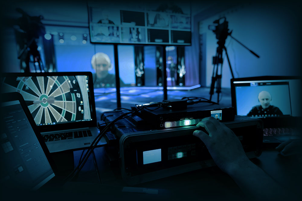 Regieraum-Szene mit Mischpult, Laptops und Kameras, während auf den Monitoren ein zugeschalteter Video-Teilnehmer und Bildsignale einer Live-Produktion zu sehen sind