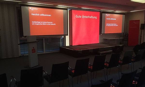 Konferenztechnik mit zwei Monitoren und ausgeleuchteter Bühne bei der Sparkasse