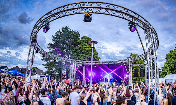 Open-Air-Konzert mit großer Menschenmenge vor einer beleuchteten Bühne unter einem runden Traversenbogen.