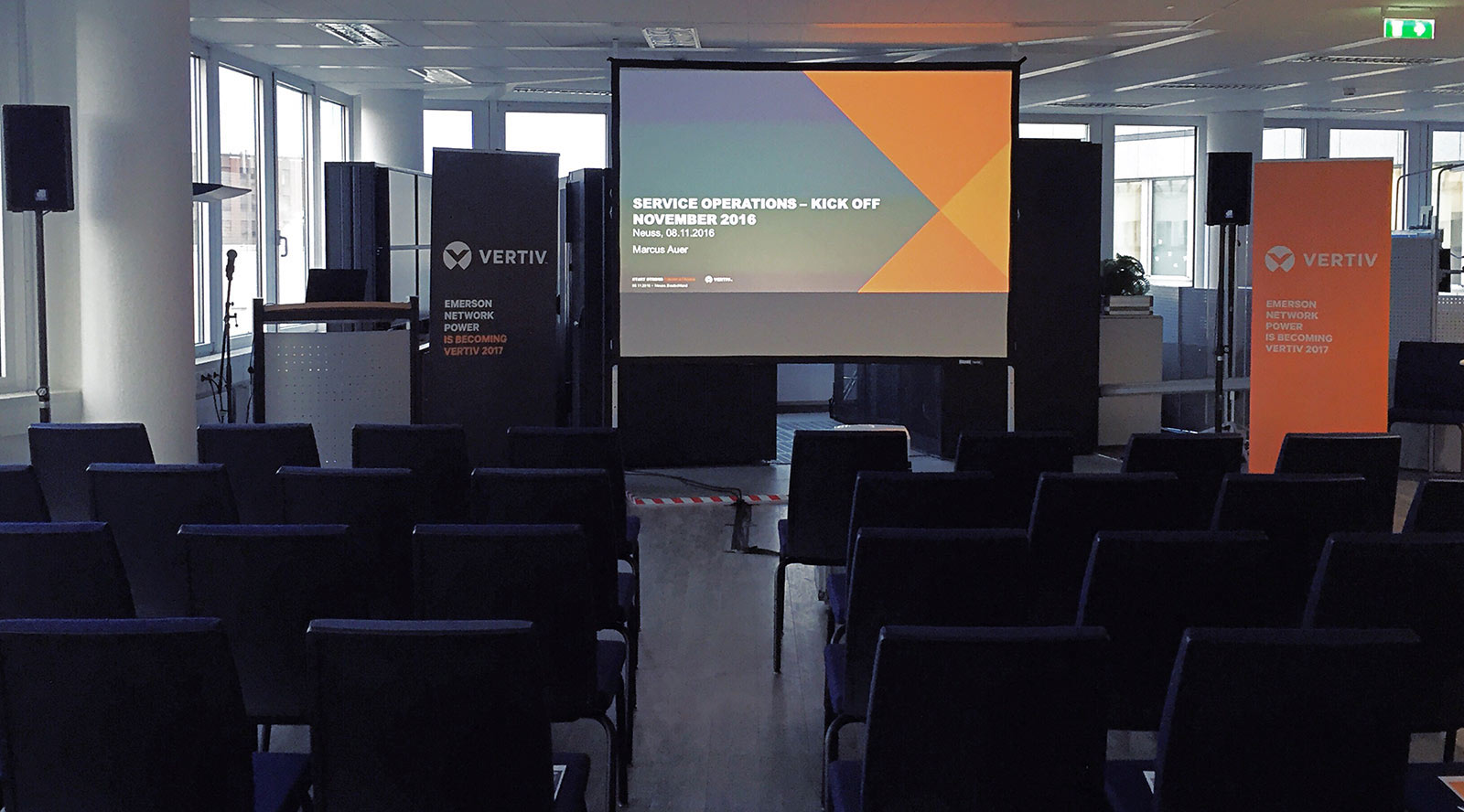 Konferenzraum mit Reihenbestuhlung, großer Projektionsfläche und Vertiv-Branding, vorbereitet für eine Präsentation