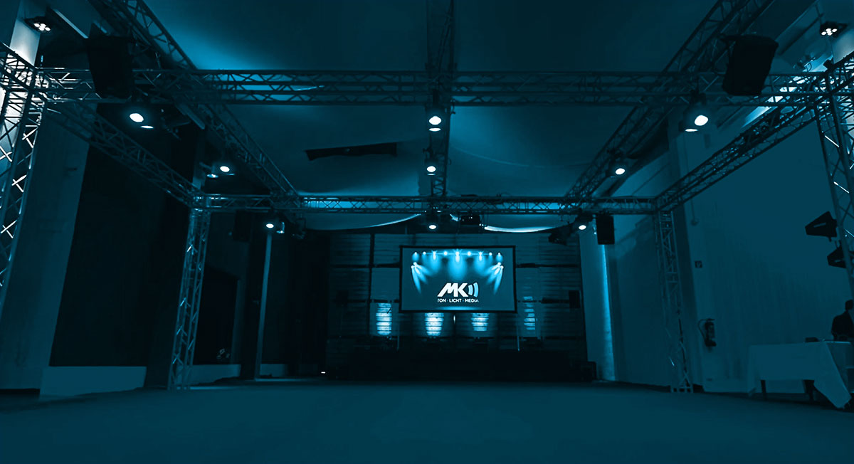 MK-SL Veranstaltungshalle mit großem Traversensystem, Bühnenbeleuchtung und zentraler Leinwand, illuminiert in blauem Licht.